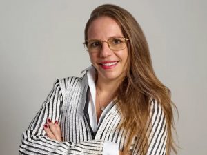 A aluna Bianca Cutait está de braços cruzados, óculos de grau e sorrindo.
